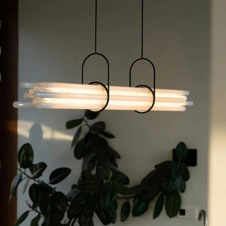 A trio of cylindrical pendant lights with warm illumination suspended above indoor plants in a dimly lit space.
