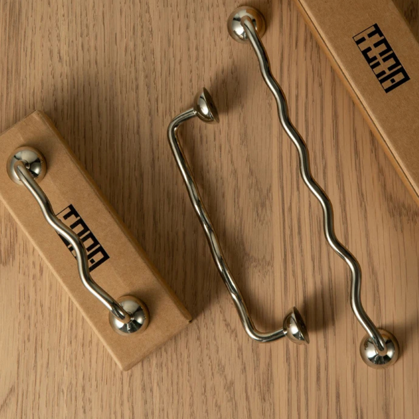 Wavy metal cabinet handles placed on a wooden surface with packaging boxes