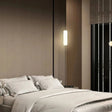 A glowing vertical pendant light suspended next to a bed in a dark-toned contemporary bedroom.
