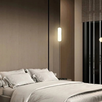 A glowing vertical pendant light suspended next to a bed in a dark-toned contemporary bedroom.
