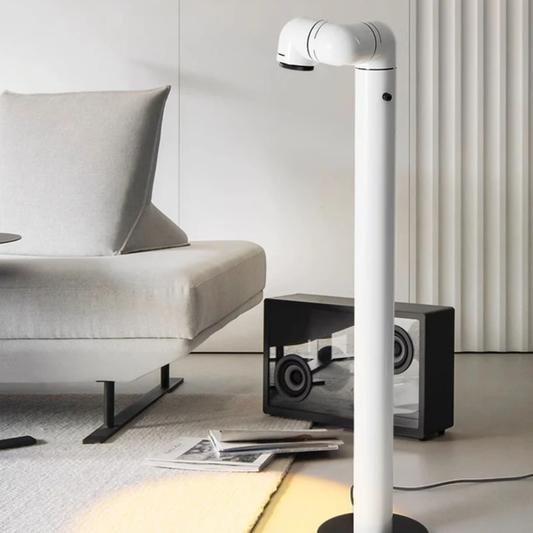 A white floor lamp with a sleek design, its light fixture angled to illuminate the space beside a chair.