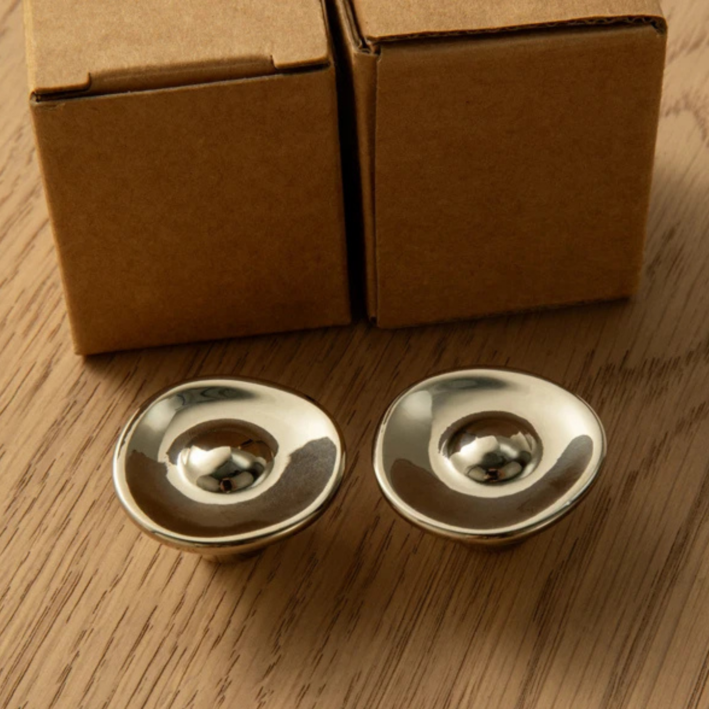Two polished metal knobs placed in front of cardboard packaging boxes