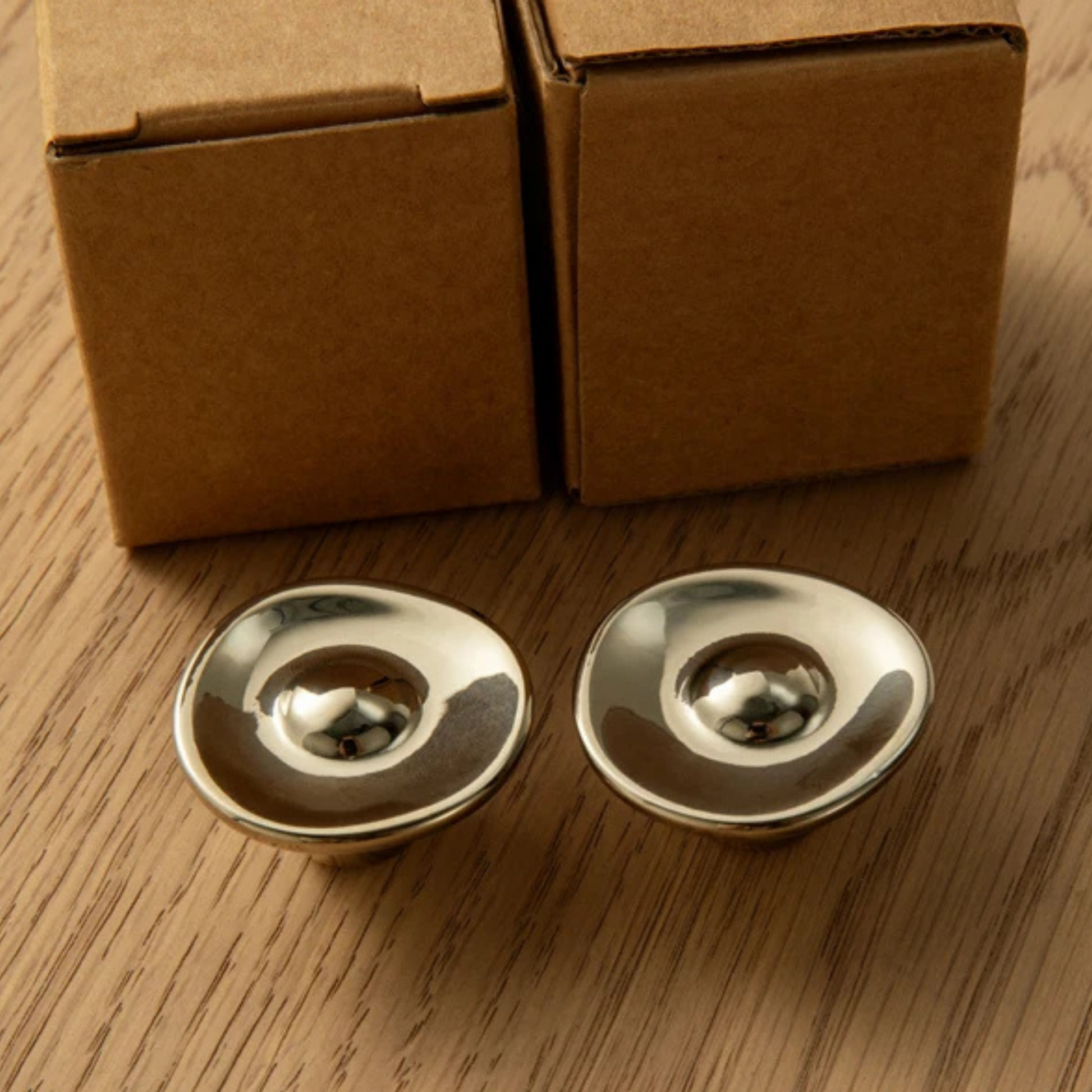 Two polished metal knobs placed in front of cardboard packaging boxes