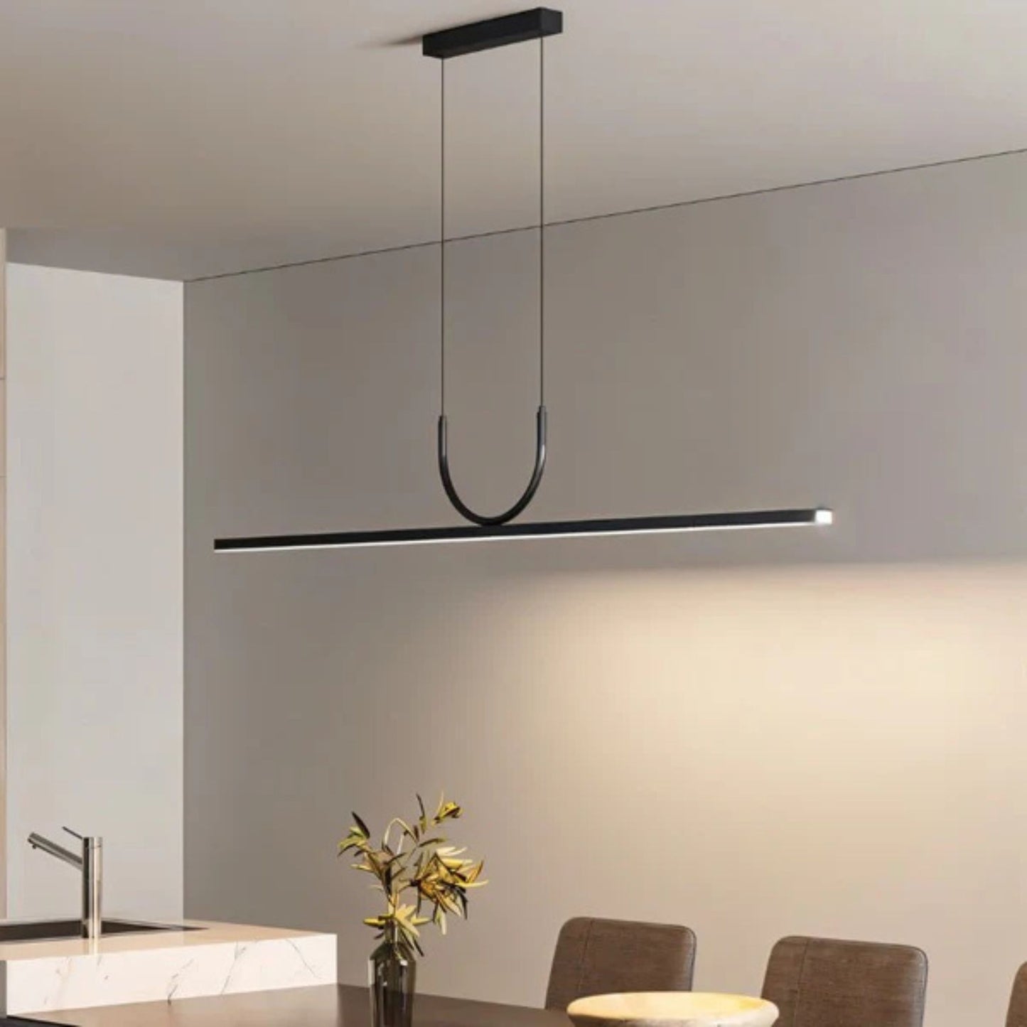 A sleek, black linear pendant light hanging above a modern kitchen table with a vase of flowers.