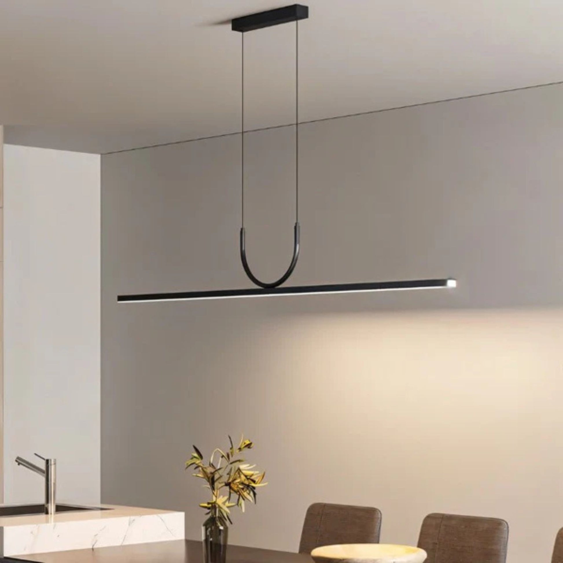A sleek, black linear pendant light hanging above a modern kitchen table with a vase of flowers.