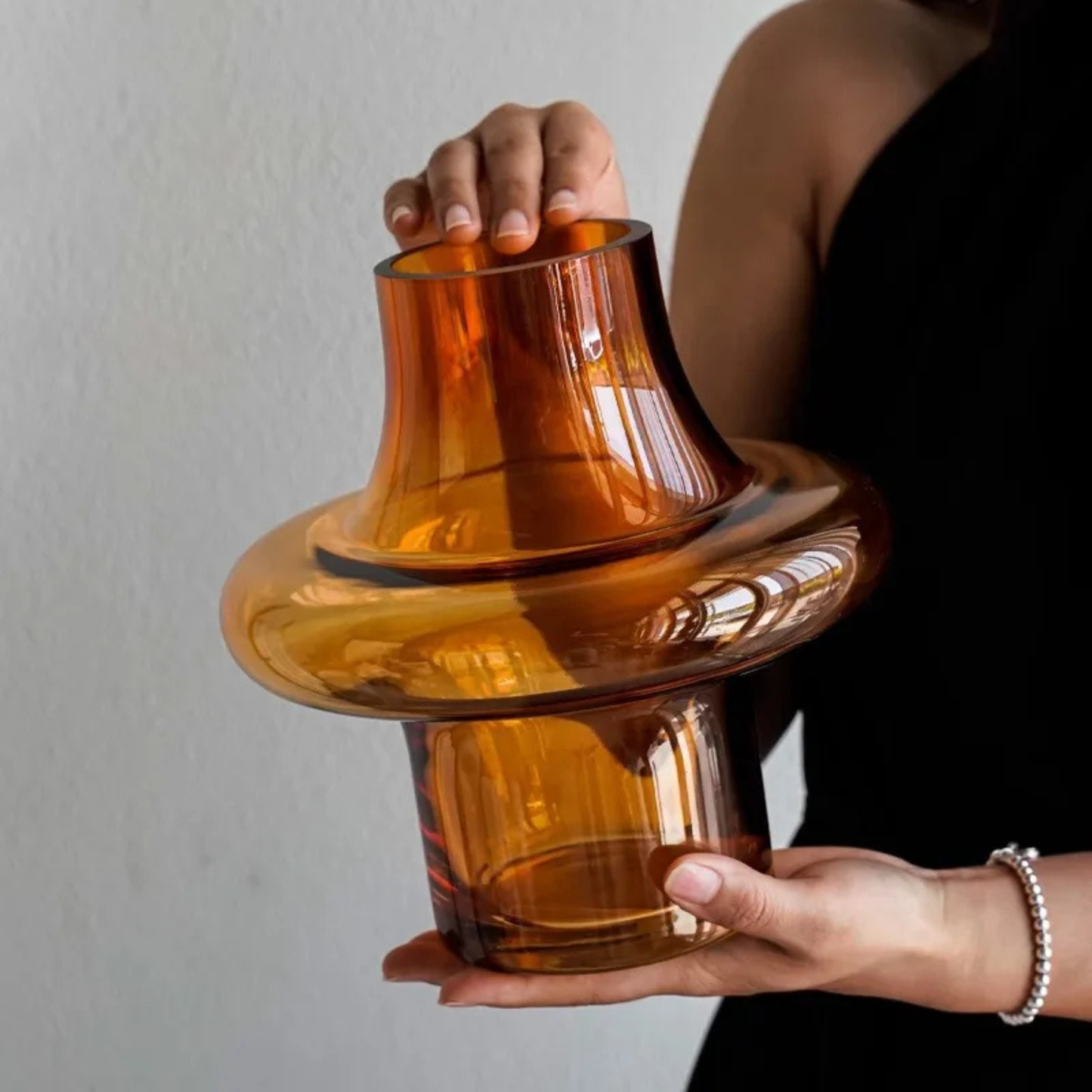Person holding a large amber glass vase with both hands, showing its transparent amber color and sculptural rounded form.