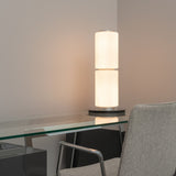 Modern ribbed-glass table lamp placed on a white desk beside a window.