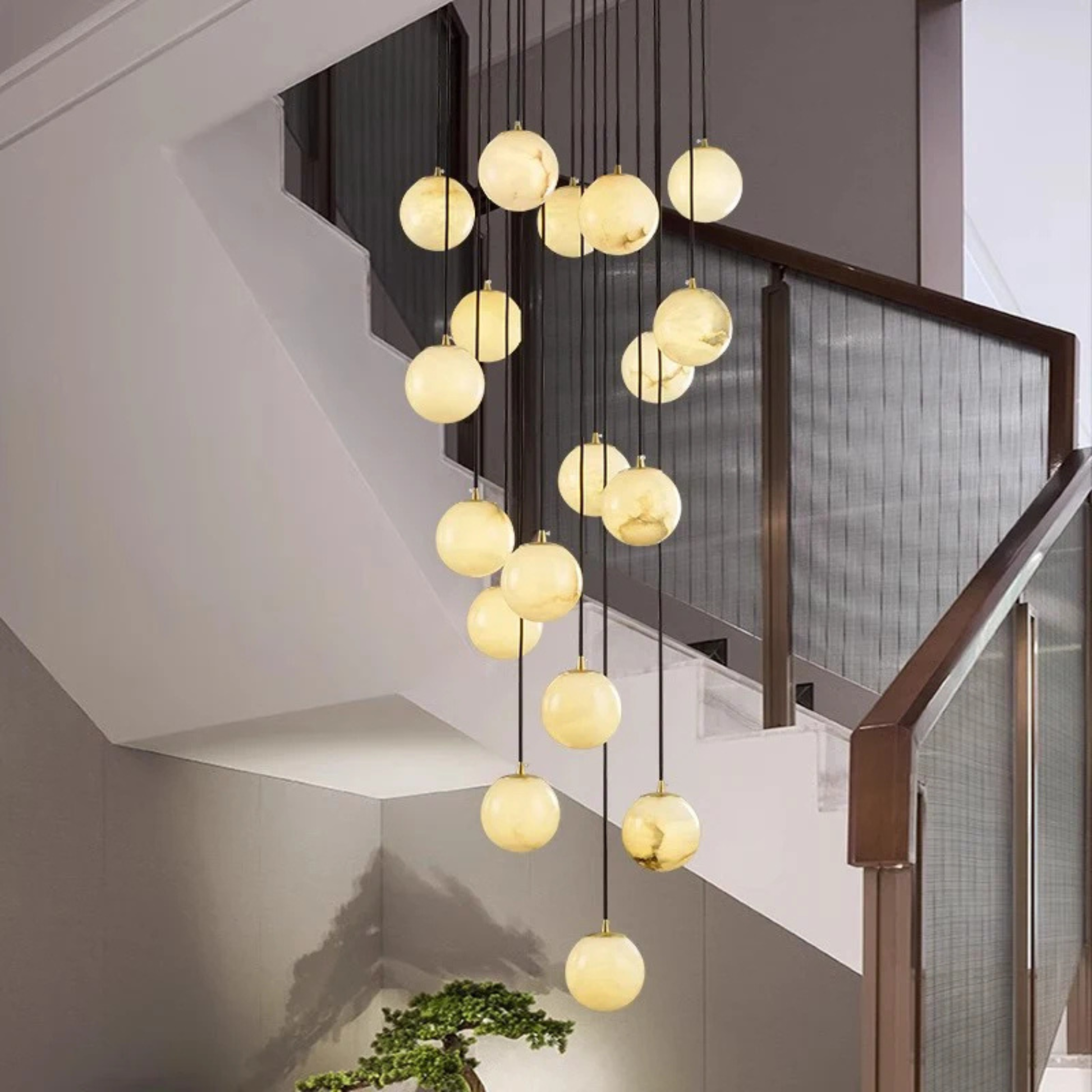 A vertical pendant light cluster with spherical lamps illuminating a stairwell with curved walls.