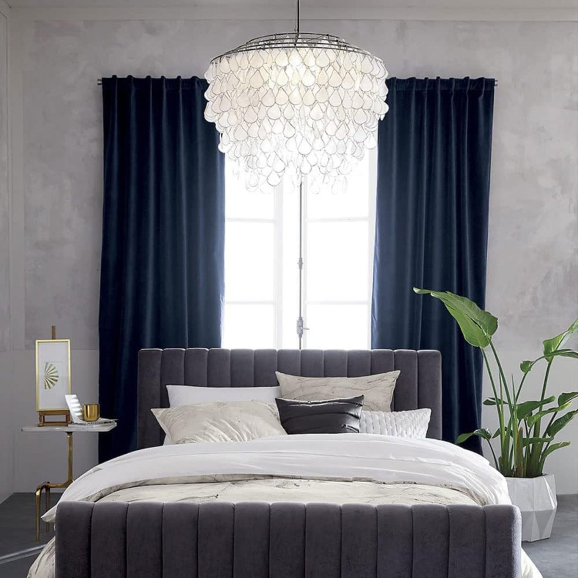 A modern bedroom featuring a tufted bed with white bedding, navy curtains, and a large, decorative pendant light hanging from the ceiling.