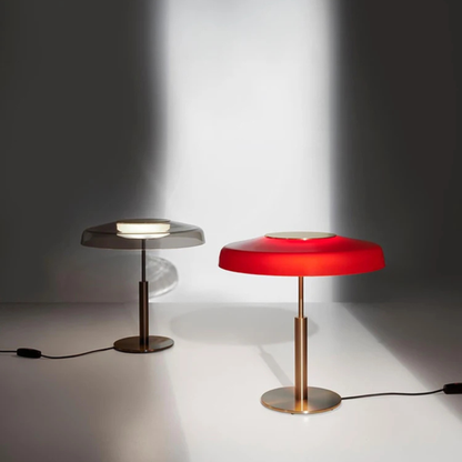 Two modern table lamps side by side  one with a silver shade and one with a bright red shade both casting light on a gray background.