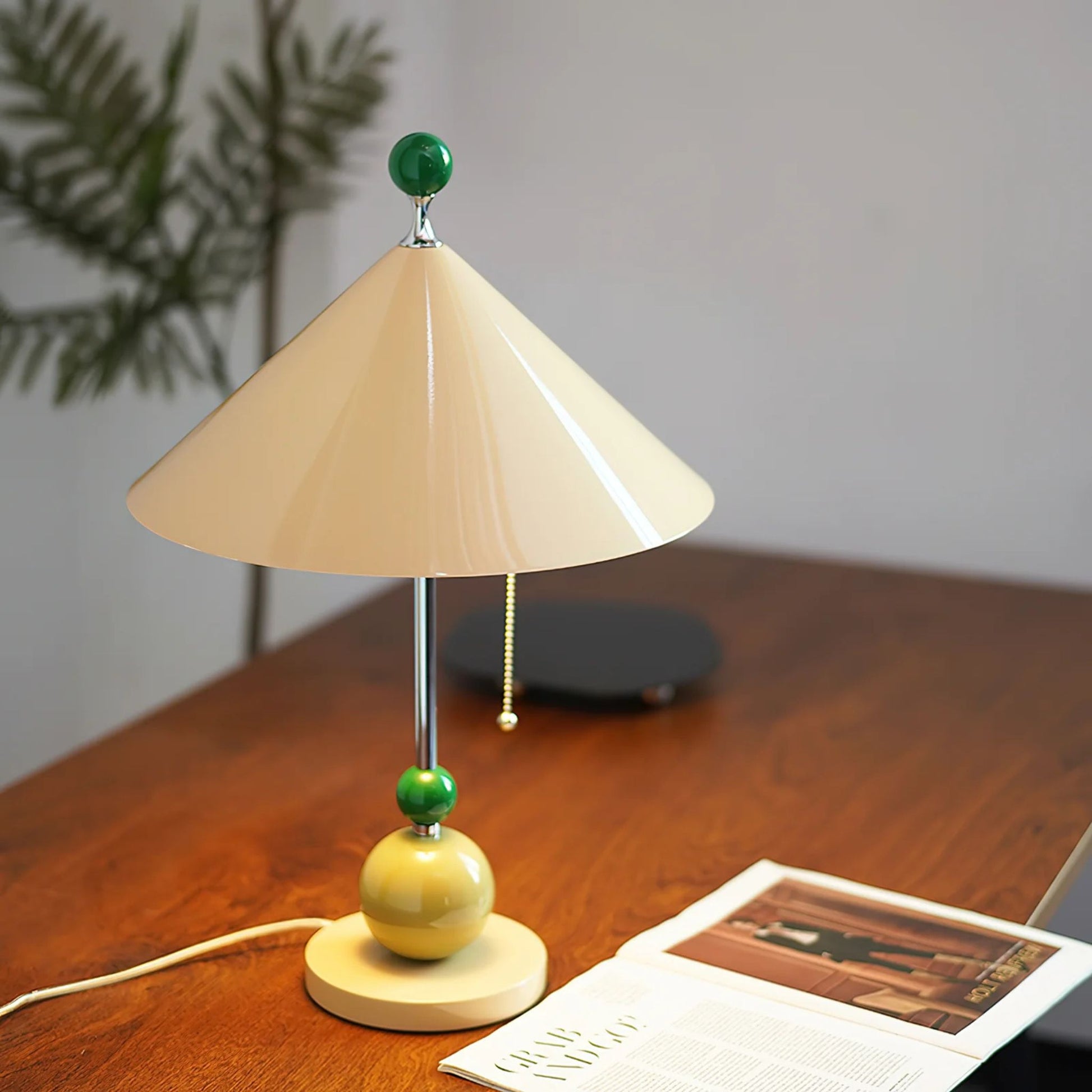 A unique table lamp with a beige cone-shaped shade and green accent balls, placed on a wooden table with a few books.