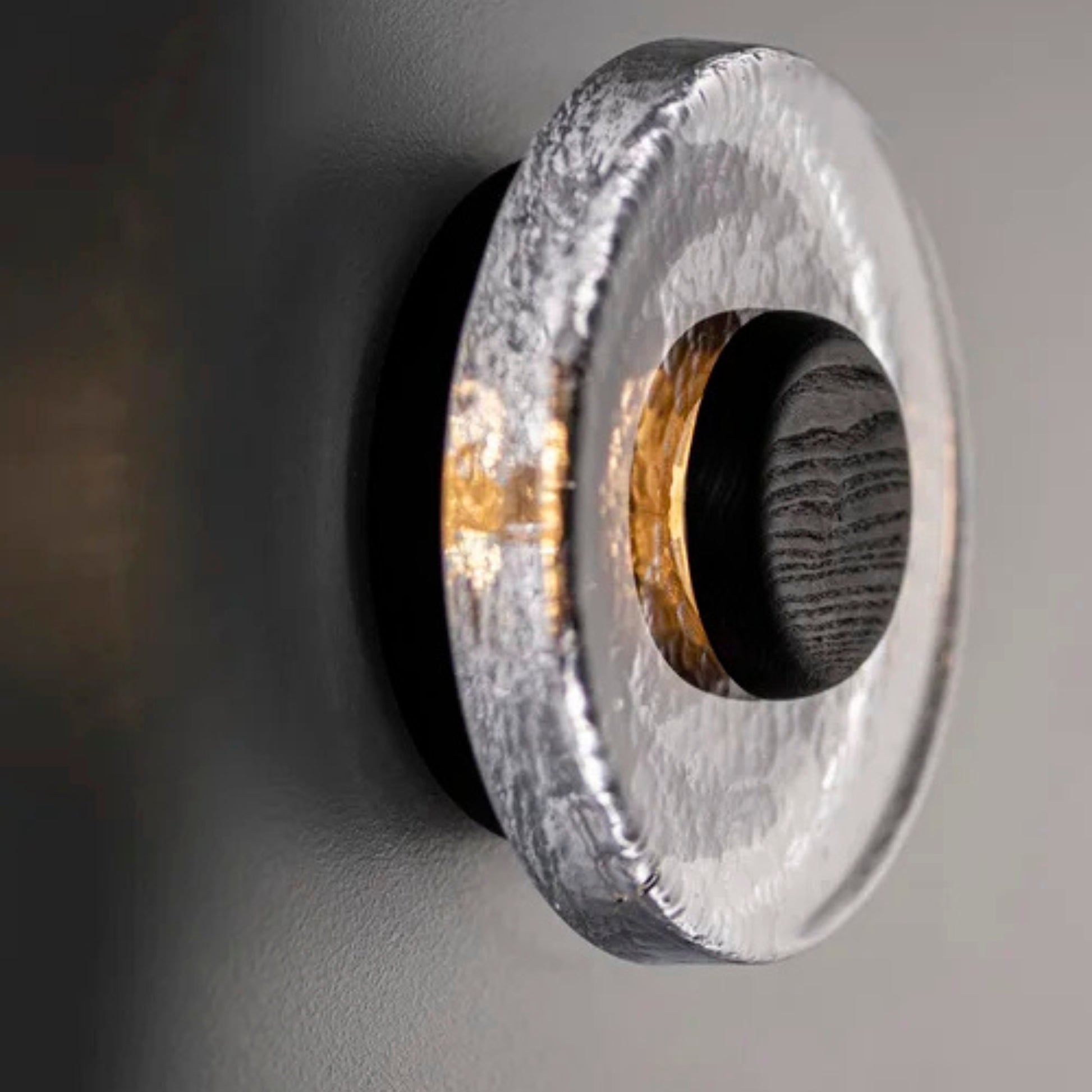 A close-up of a round wall light with a textured stone-like outer ring and a dark inner core mounted on a dark wall.