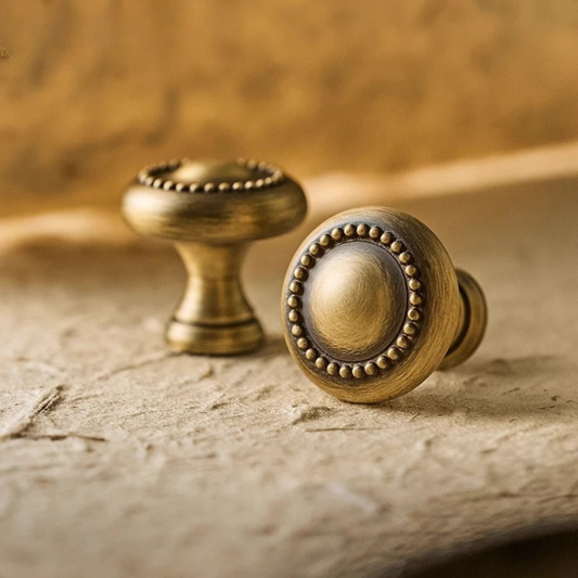 A pair of round antique gold cabinet knobs installed on white cabinet doors.