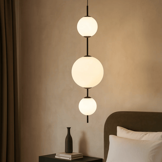 Modern pendant light fixture in a bedroom setting with neutral walls and bedding.