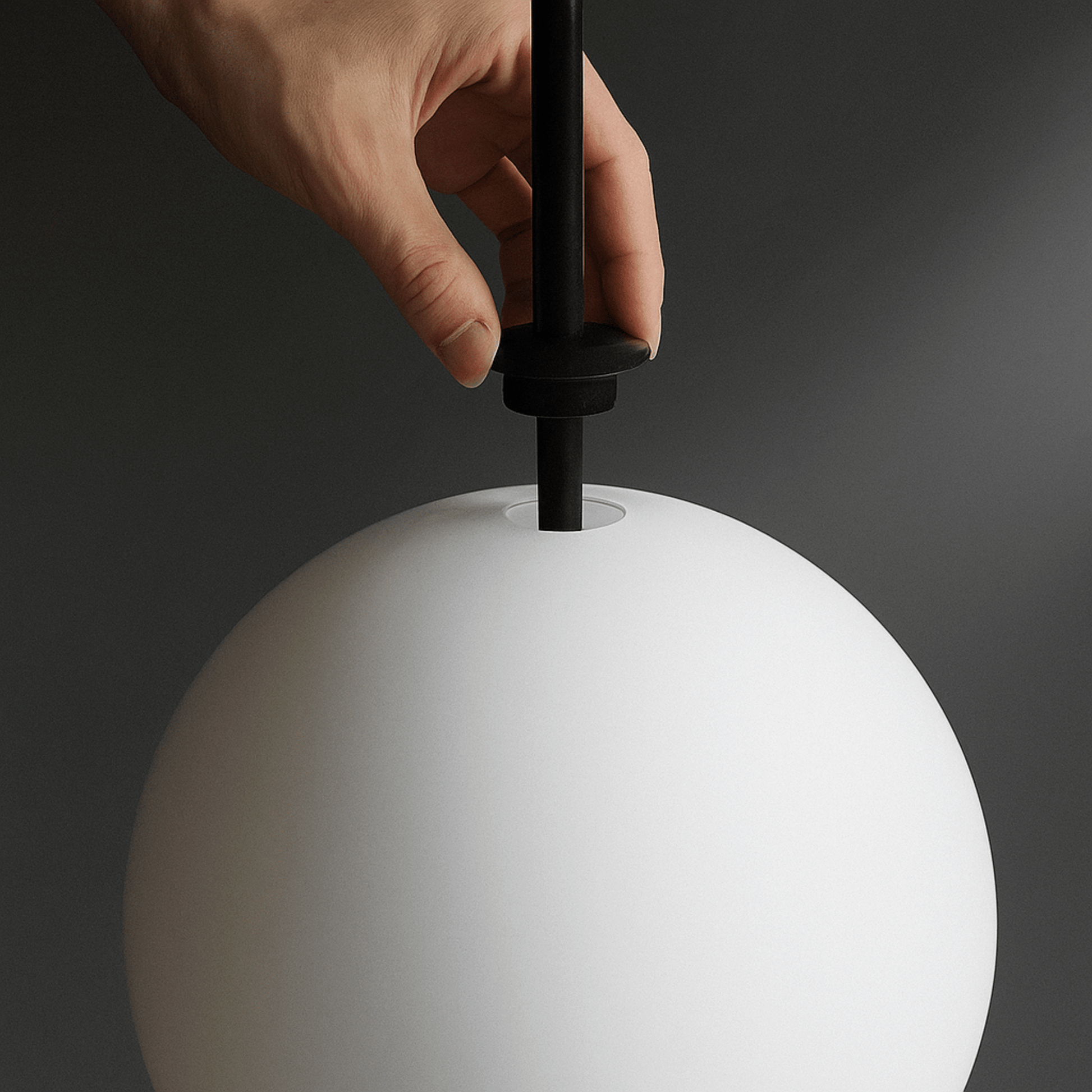 Hand adjusting a black fixture on a white spherical object against a dark background
