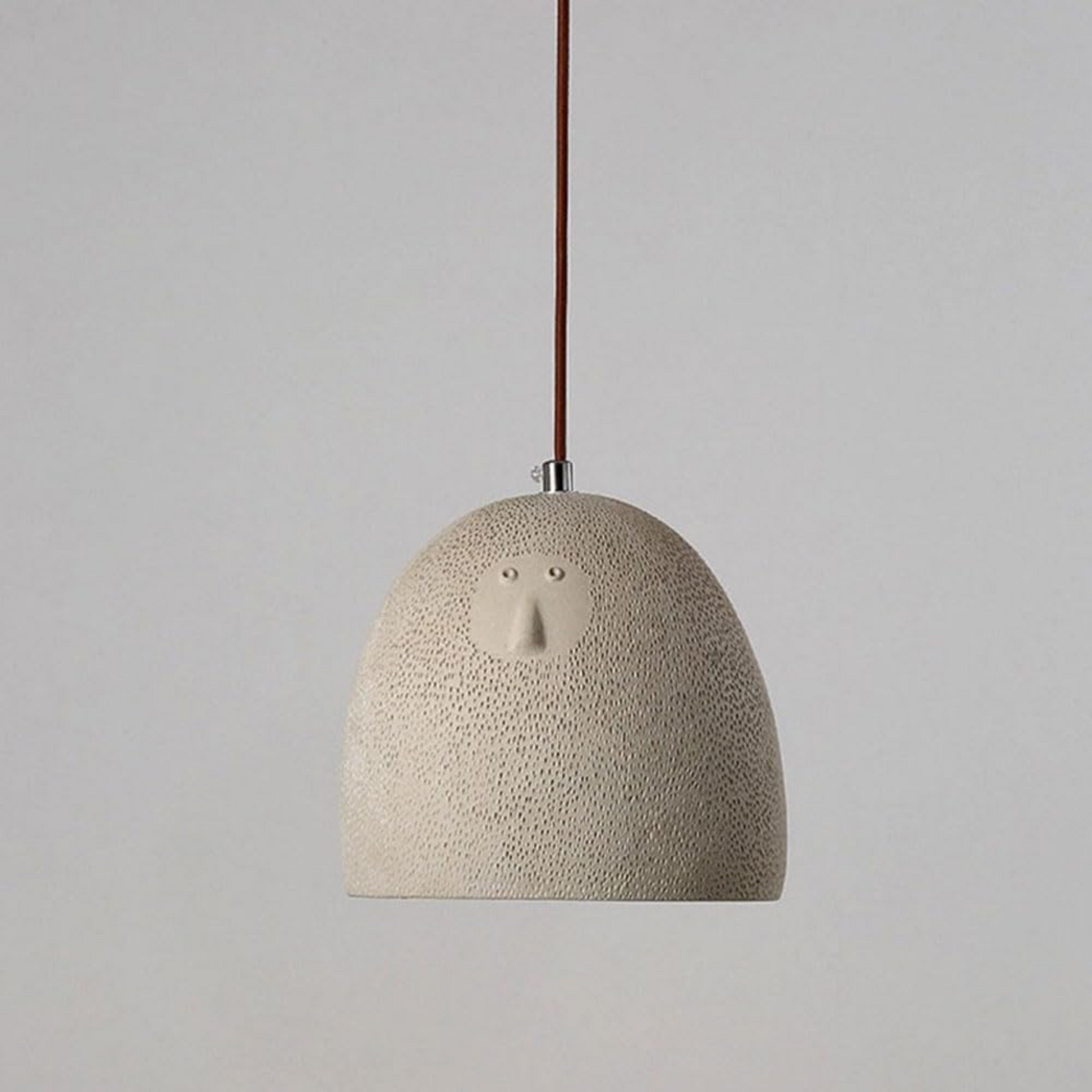 Textured pendant light with a face design on a plain background