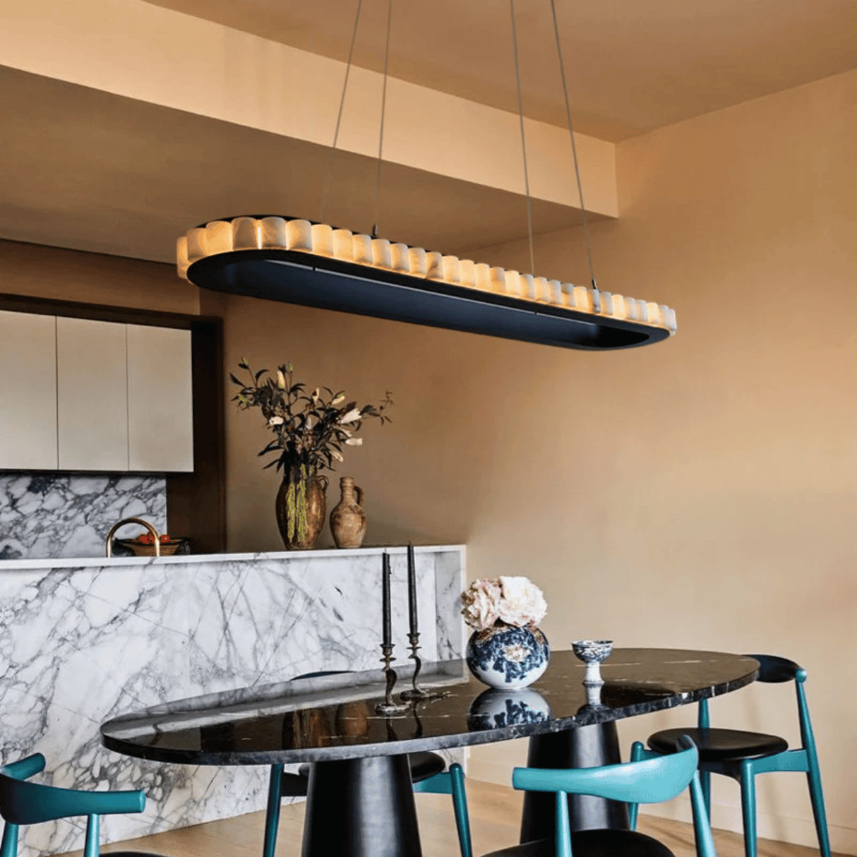 Modern kitchen with a black dining table and chairs, marble countertop, and pendant light.