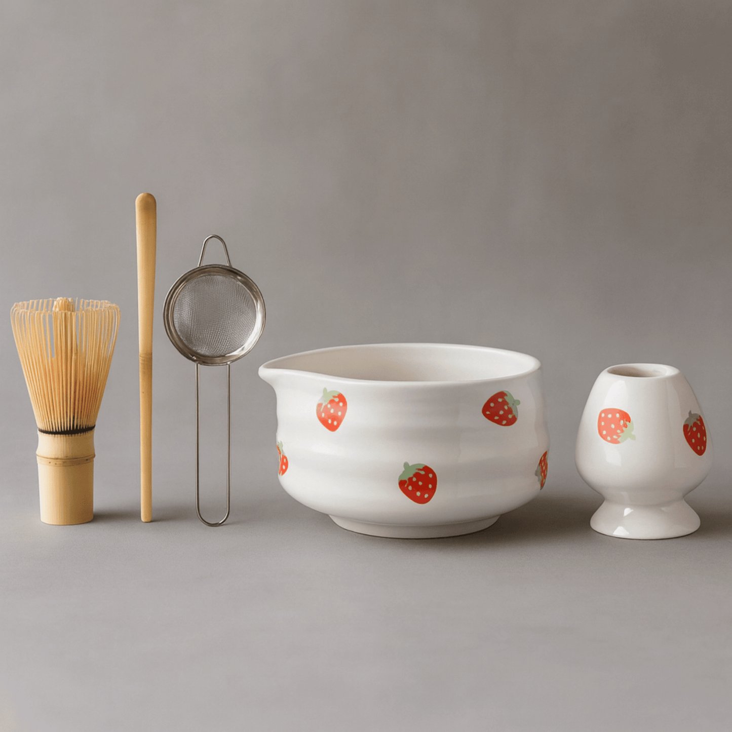 Ceramic bowl with strawberry pattern, whisk, and other tea-making tools on a gray background