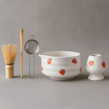 Ceramic bowl with strawberry pattern, whisk, and other tea-making tools on a gray background