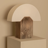 Table lamp with marble base and white shade on a beige pedestal against a beige wall.