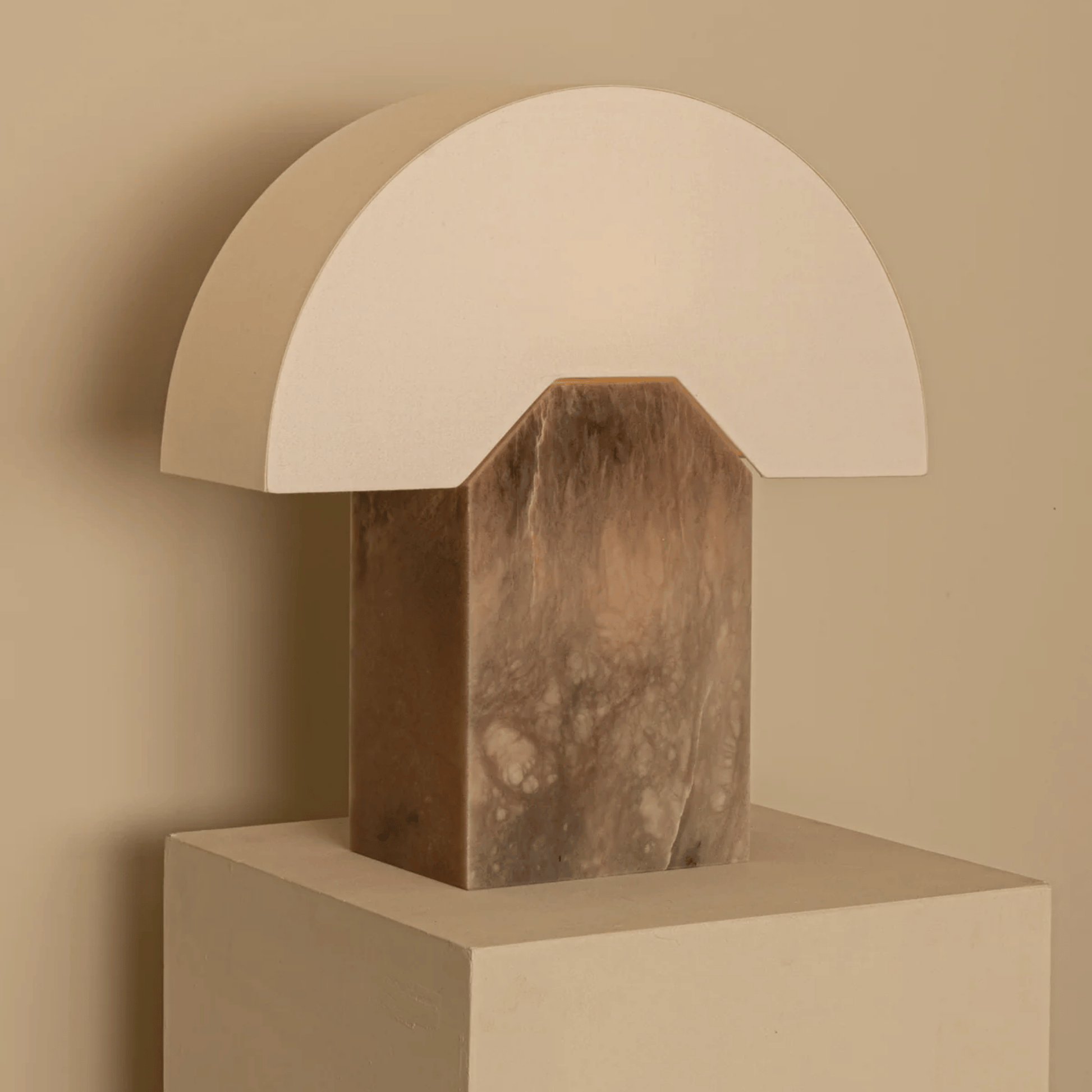 Table lamp with marble base and white shade on a beige pedestal against a beige wall.