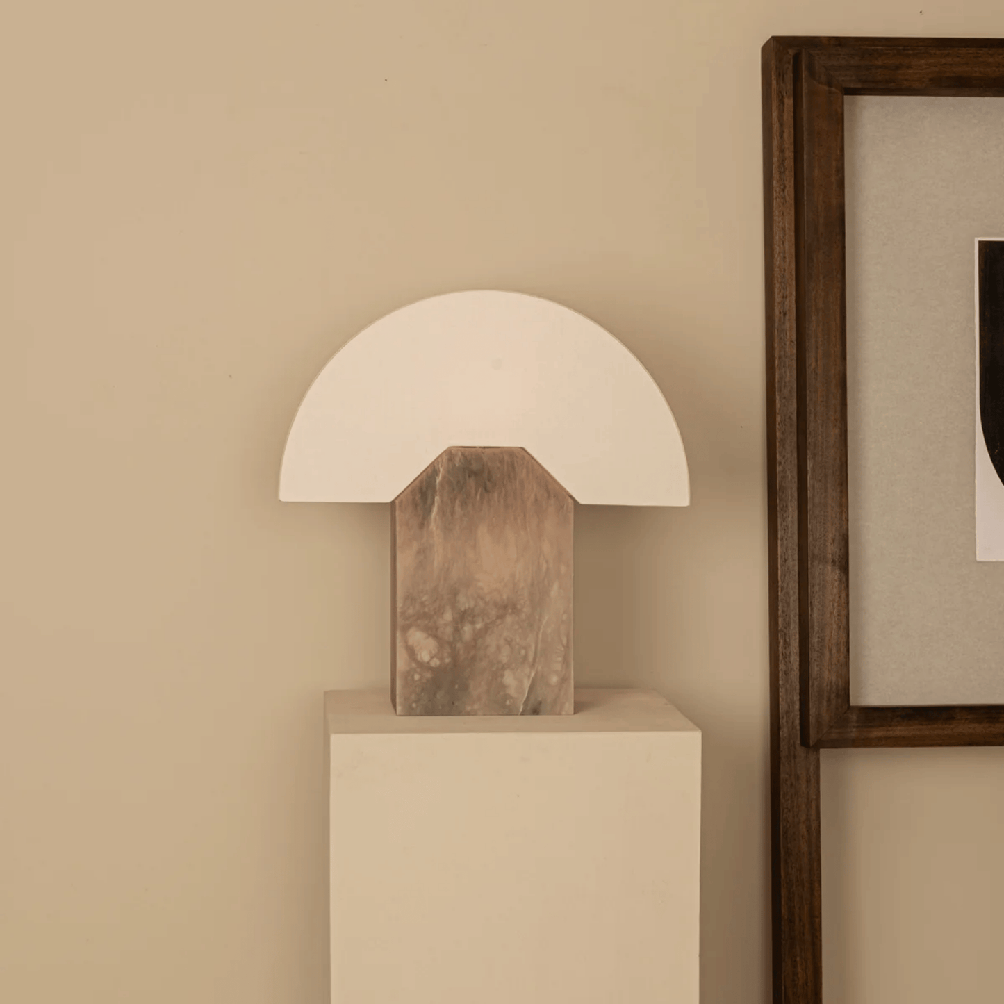 Table lamp with wooden base on a white pedestal against a beige wall.