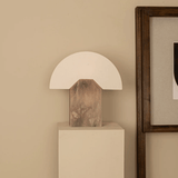 Table lamp with wooden base on a white pedestal against a beige wall.