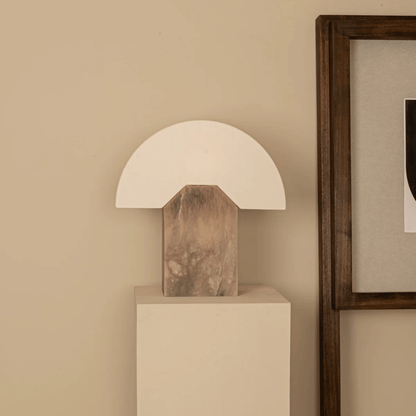 Table lamp with wooden base on a white pedestal against a beige wall.