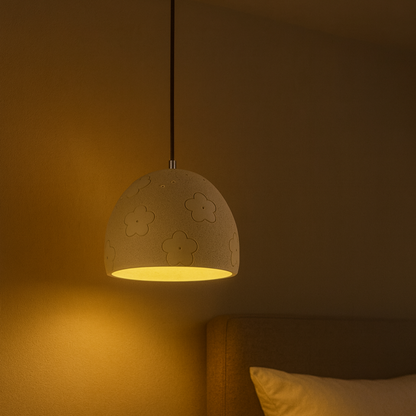 Cement pendant light with floral patterns on a warm-toned wall.