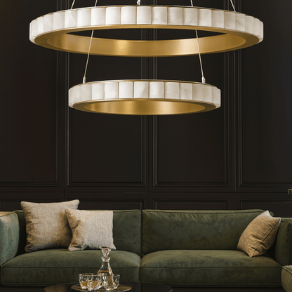 Modern chandelier hanging above a green sofa with decorative pillows against a dark wall.