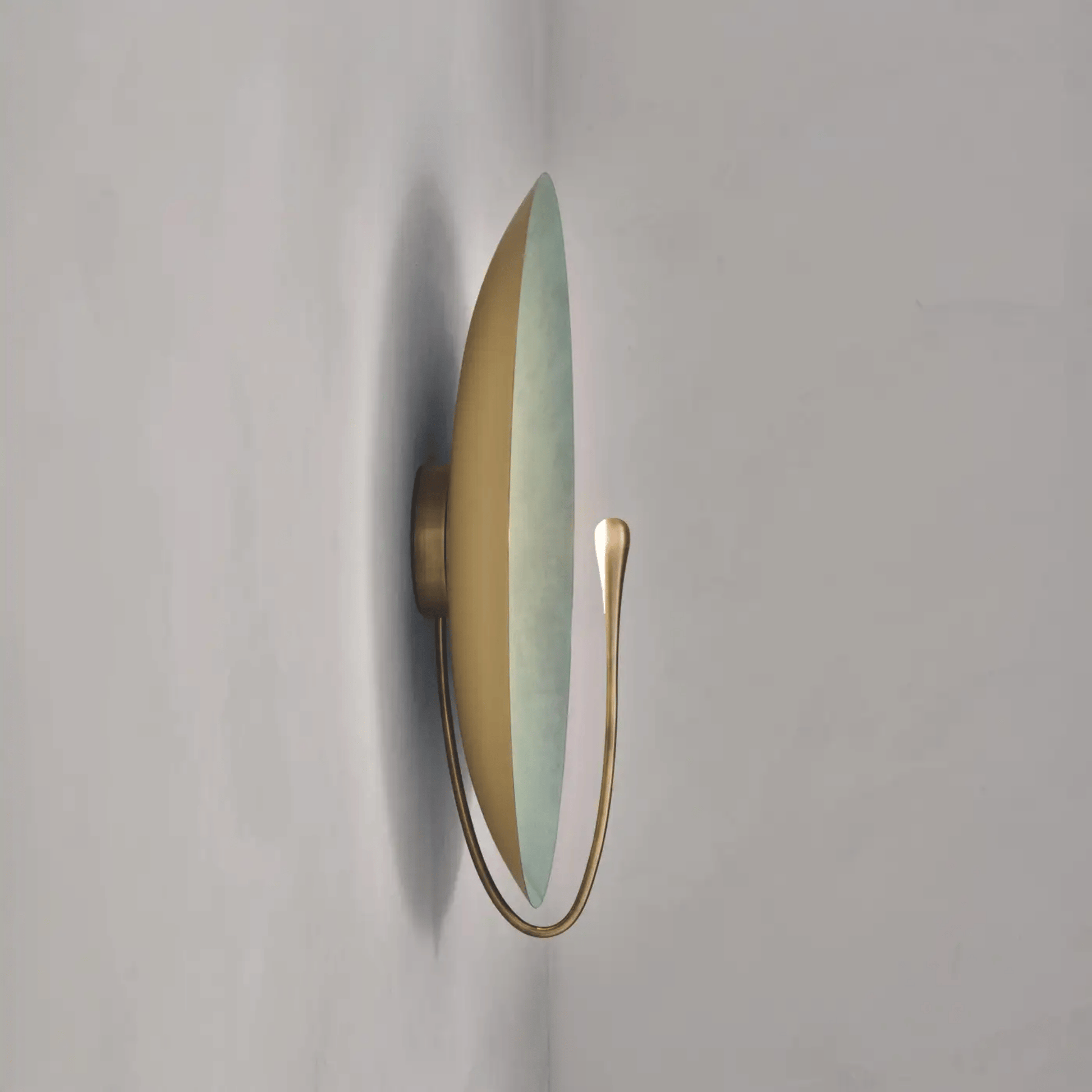 Wall-mounted light fixture with gold frame and green glass on a white background