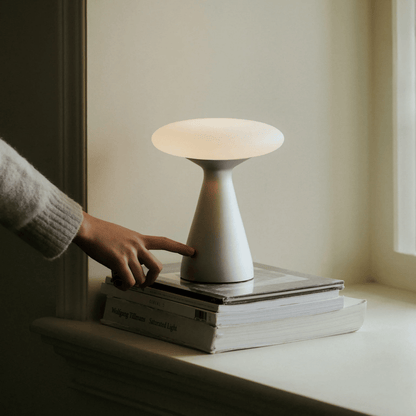 Person adjusting a small lamp on a stack of books in a softly lit room.