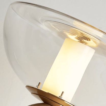 Wall-mounted light fixture with clear glass shade and gold metal base on a white background