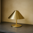 Gold table lamp on a dark surface with a beige wall background