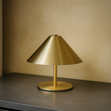 Gold table lamp on a dark surface with a beige wall background