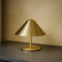Gold table lamp on a dark surface with a beige wall background