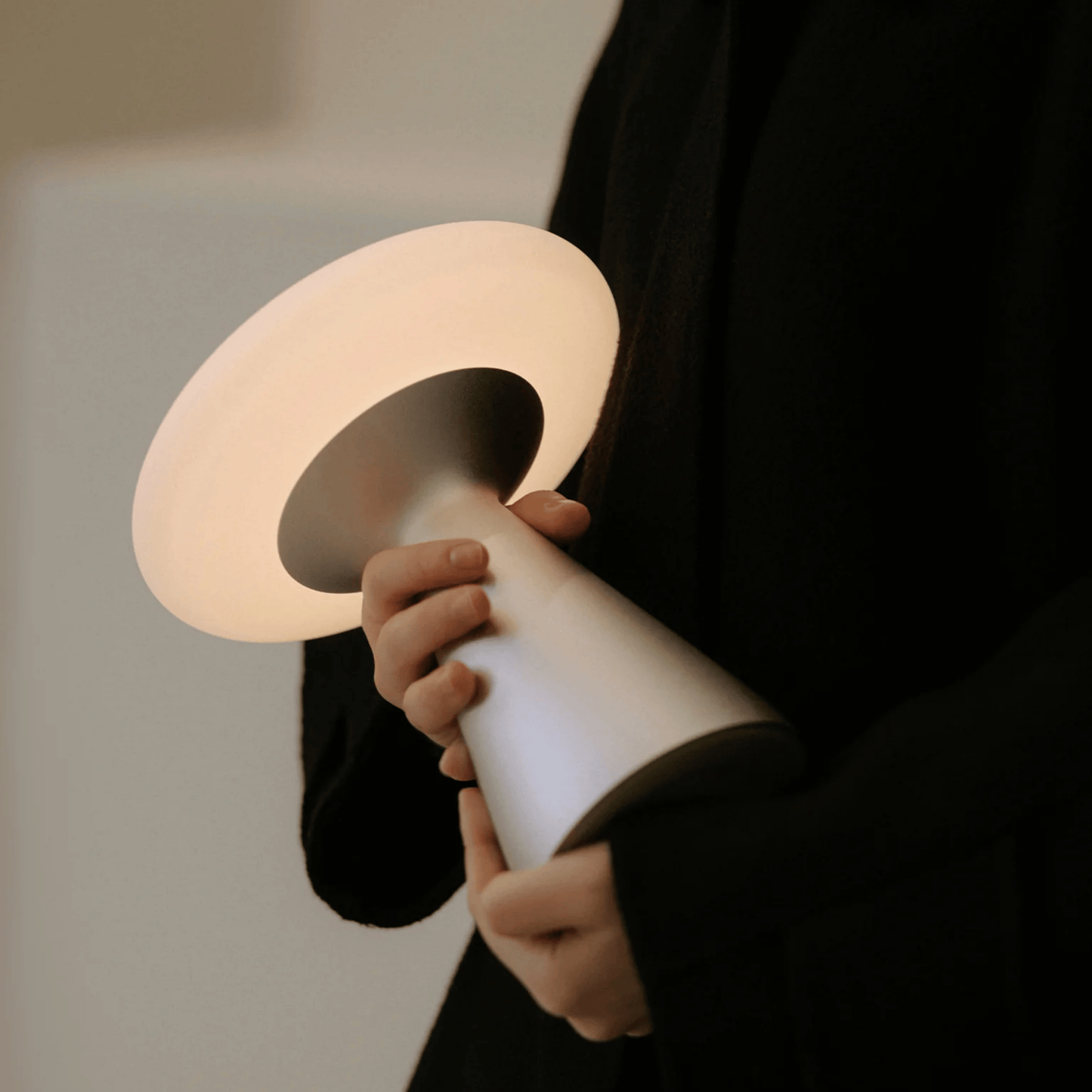 Person holding a modern, curved lamp with a soft glow against a neutral background