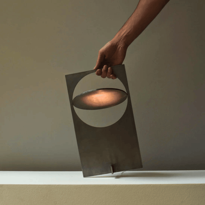 Hand holding a modern metal lantern with a warm glow against a neutral background