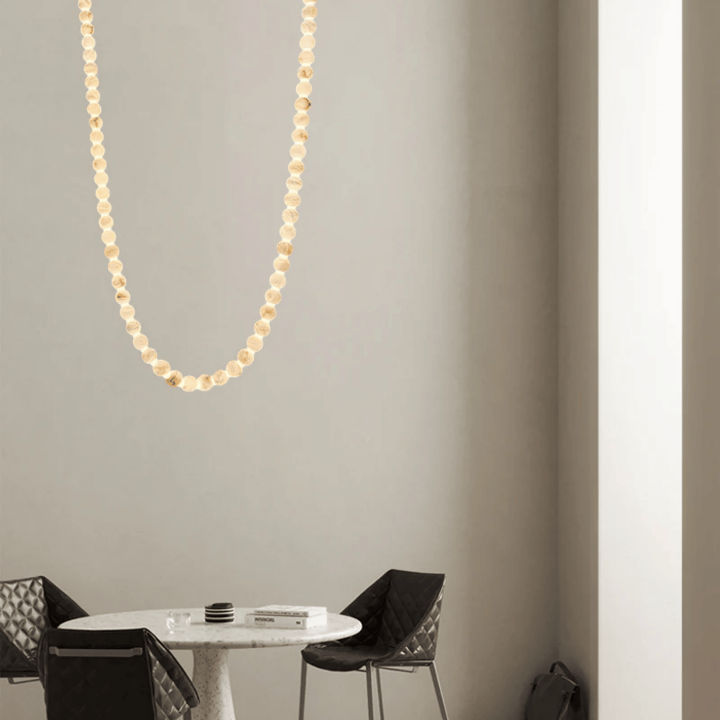 Gold necklace hanging on a gray wall above a round table with chairs.