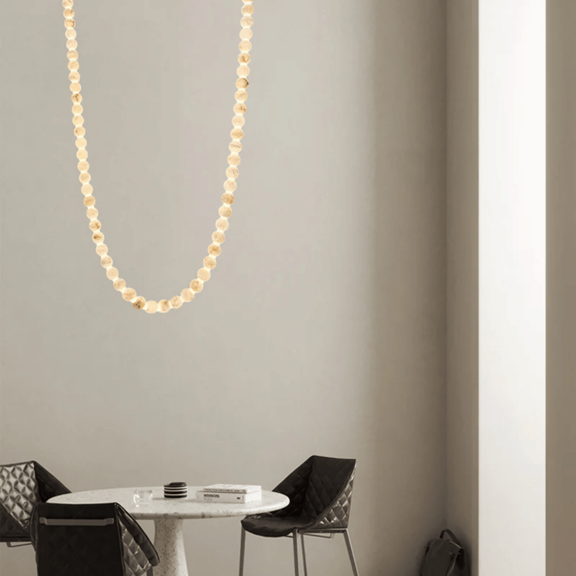 Gold necklace hanging on a gray wall above a round table with chairs.