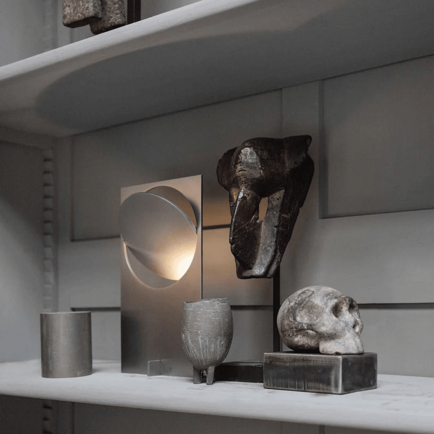Decorative shelf with abstract sculptures and a metallic lamp against a neutral background