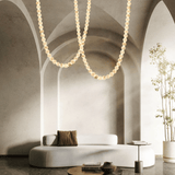 Modern living room with a white sofa, decorative pillows, and a hanging pearl necklace-like light fixture.