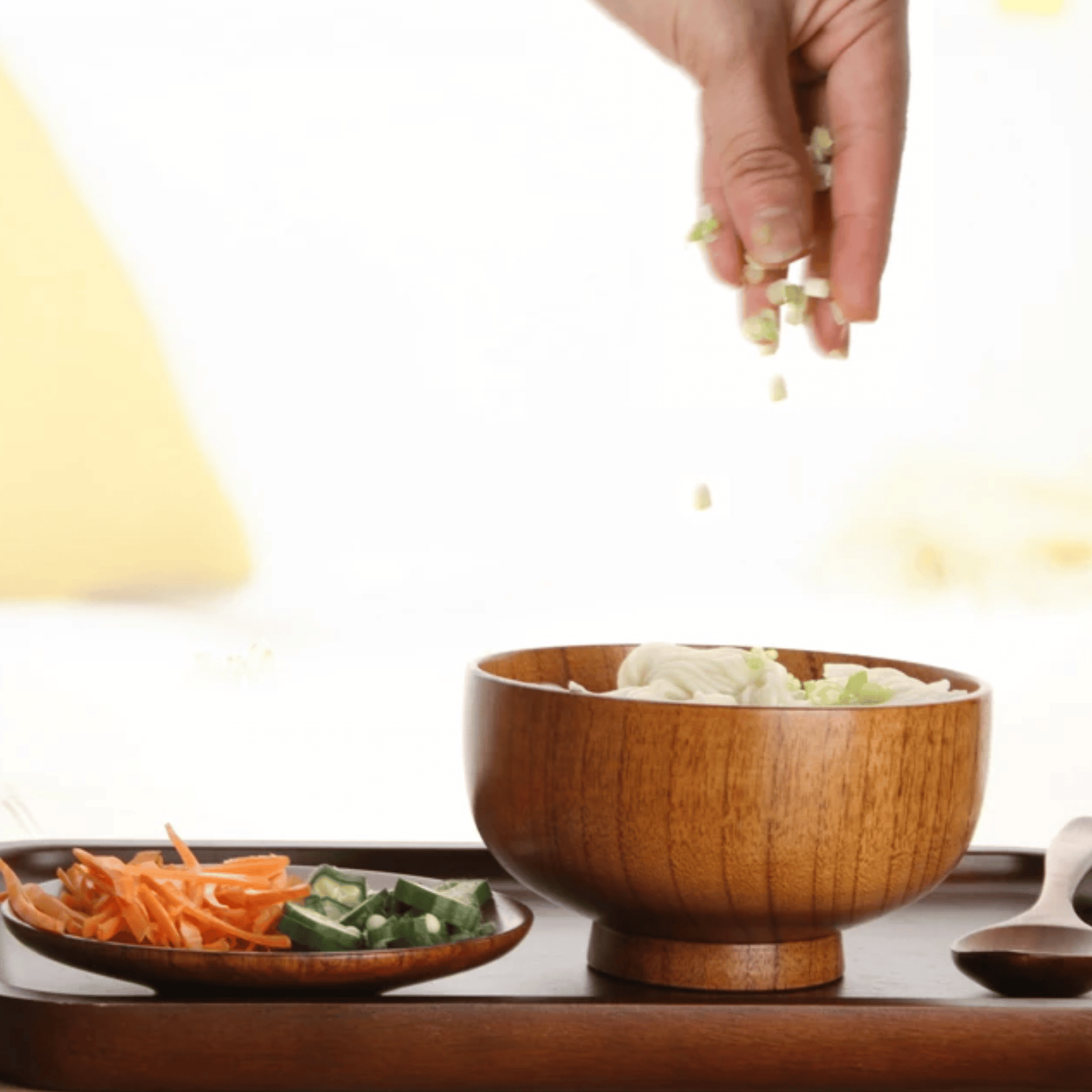 Wooden bowl with salad on a table, hand adding ingredients