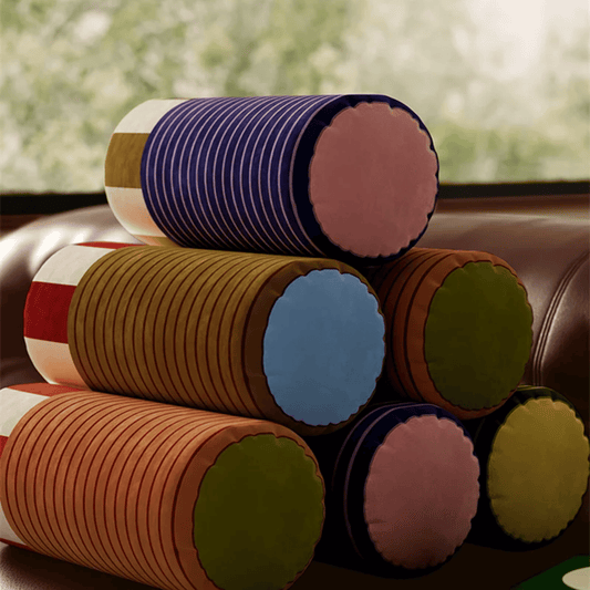 Stack of colorful cylindrical pillows on a couch with a blurred window background