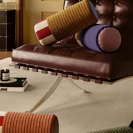 Brown leather bench with colorful cylindrical cushions on a beige carpet.