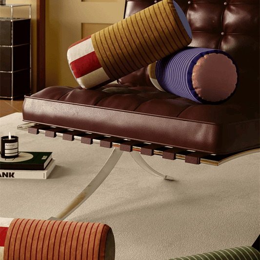 Brown leather bench with colorful cylindrical cushions on a beige carpet.