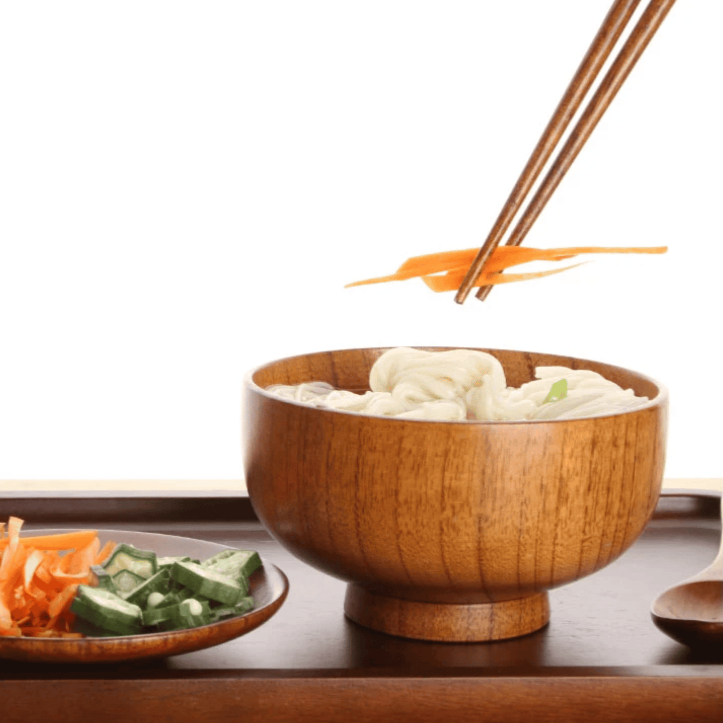 Wooden bowl of noodles with chopsticks and side dishes on a wooden table
