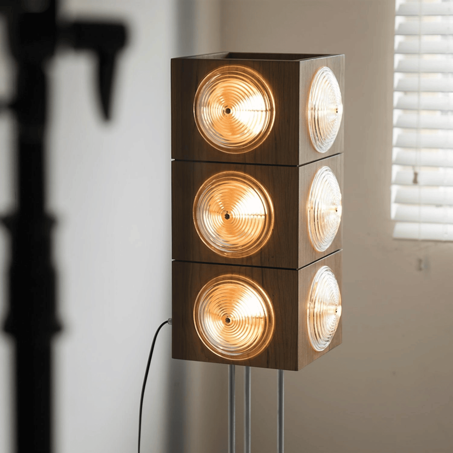 Modern floor lamp with four cylindrical lights stacked vertically against a neutral wall.