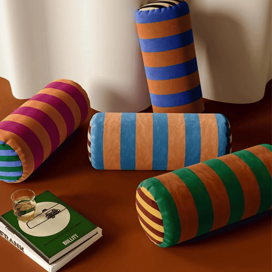 Colorful striped cylindrical pillows on a wooden surface with a book and glass.