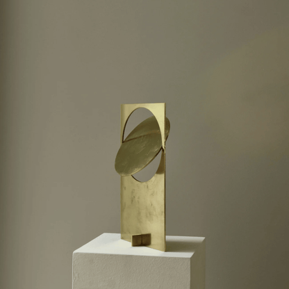 Gold abstract sculpture on a white pedestal against a beige background